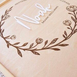 May include: A wooden sign with a floral wreath design, the name "Noah" in white lettering, and the text "Mark Williams" and "3:05 AM" below.