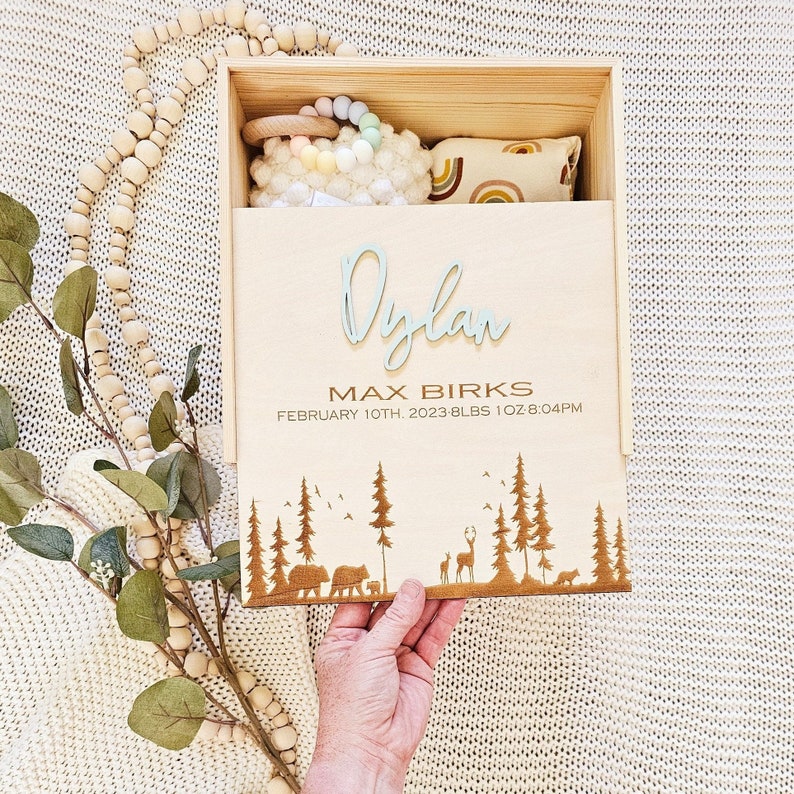 May include: Wooden keepsake box with a light blue engraved name "Dylan" and the text "Max Birks, February 10th, 2023, 8 lbs 1 oz, 8:04 PM". The box has a forest scene with trees, birds, and deer engraved on the bottom.