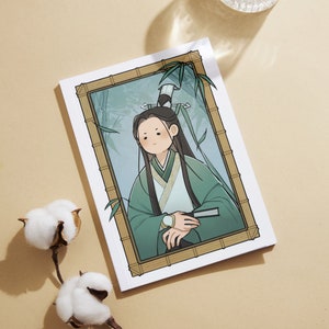Op de afbeelding: Een ingelijste illustratie van een persoon met lang zwart haar die een groene en witte robe draagt. De persoon staat in een bamboebos. De lijst is van hout en heeft een lichtbruine kleur.