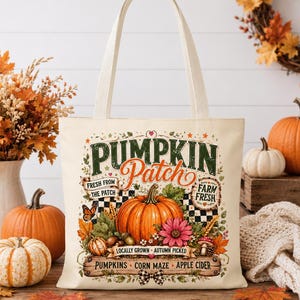 Peut inclure: Un sac fourre-tout en toile couleur crème avec une impression graphique colorée représentant un champ de citrouilles. Le motif inclut le texte PUMPKIN PATCH, FRESH FROM THE PATCH, FARM FRESH, PUMPKINS, CORN MAZE et APPLE CIDER, entouré de citrouilles.