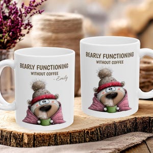 May include: Two white ceramic mugs with the text "BEARLY FUNCTIONING WITHOUT COFFEE" and a cartoon bear wearing a hat and scarf. The bear is holding a green mug. One mug has the name "- Emily" below the text.