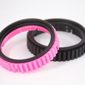May include: Two camera lens rings, one black and one pink with a black inner ring. Both rings have a textured outer edge.