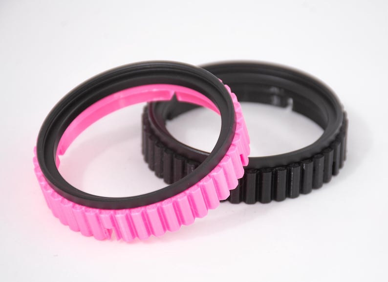 May include: Two camera lens rings, one black and one pink with a black inner ring. Both rings have a textured outer edge.