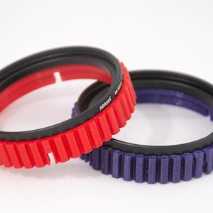 May include: Two camera lens filter rings, one red and one purple, with a black rubber ring and a gear-like edge.