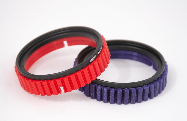May include: Two camera lens filter rings, one red and one purple, with a black rubber ring and a gear-like edge.