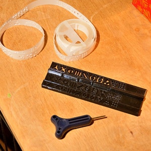 K&ouml;nnte beinhalten: Ein schwarzes Plastikwerkzeug mit erhabenen Buchstaben und Zahlen, eine wei&szlig;e Plastikspole mit Braille-Band und ein blaues Plastikwerkzeug mit T-f&ouml;rmigem Griff.