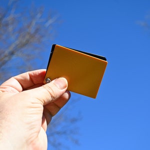 Puede incluir: Una mano sostiene una peque&ntilde;a tarjeta de muestra de color naranja contra un cielo azul.