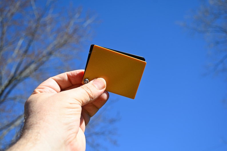 Puede incluir: Una mano sostiene una peque&ntilde;a tarjeta de muestra de color naranja contra un cielo azul.