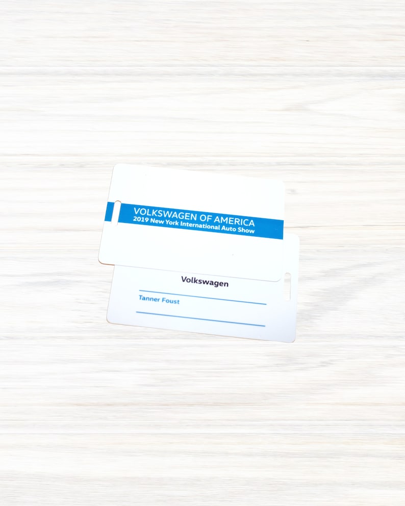 May include: White badge with blue text that reads "VOLKSWAGEN OF AMERICA 2019 New York International Auto Show". Below is a white badge with the text "Volkswagen" and a blank line for a name. The text "Tanner Foust" is written on the line.