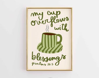 May include: A framed art print with a cream background features a green coffee cup and saucer, with steam rising from the cup. The text "my cup overflows with blessings" is written in green script. The print is in a gold frame.