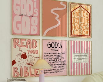 May include: A collection of framed art prints with inspirational quotes and religious themes. The prints feature pink and gold frames, with text like "God is Good" and "Read Your Bible." A small lamp sits on a white cabinet below the prints.