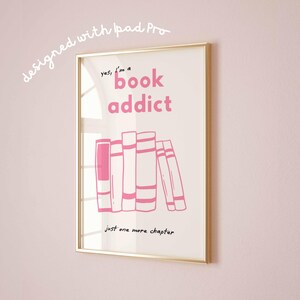 May include: A framed print with a gold border, featuring the text "yes, I'm a book addict" in pink, along with an illustration of stacked books. The phrase "Just one more chapter" is written below the books. The words "designed with iPad Pro" are written in the upper left corner.