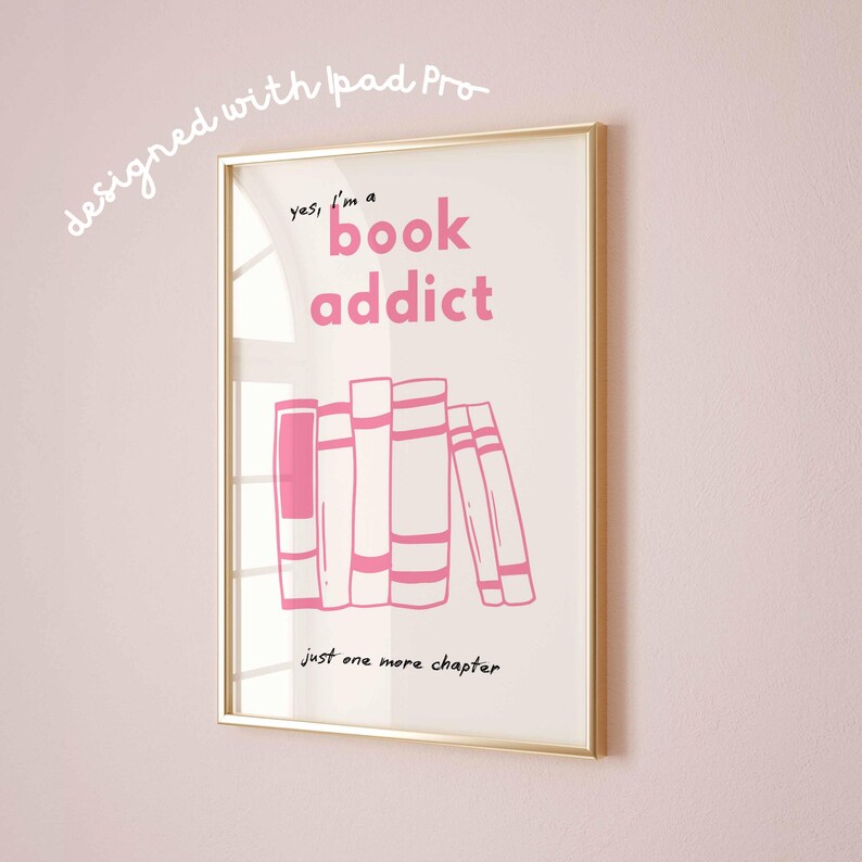 May include: A framed print with a gold border, featuring the text "yes, I'm a book addict" in pink, along with an illustration of stacked books. The phrase "Just one more chapter" is written below the books. The words "designed with iPad Pro" are written in the upper left corner.