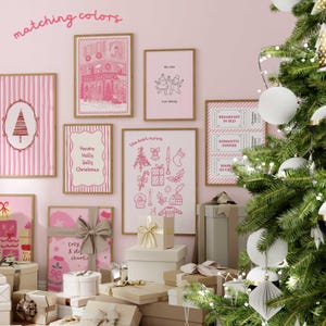 May include: A collection of framed pink and white Christmas-themed art prints and gift boxes. The prints feature festive illustrations and text, including "Have a Holly Jolly Christmas" and "the best mood". A decorated Christmas tree with white ornaments is in the background.