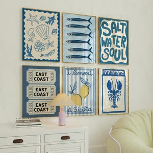 Puede incluir: Seis impresiones enmarcadas con un tema náutico. Las impresiones presentan ilustraciones de conchas marinas, peces, limones, una langosta y boletos que dicen "Costa Este". Las impresiones están en un esquema de color azul claro y amarillo.