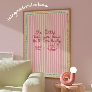 May include: A framed art print with a pink and cream striped background. The text reads "the little that you have He'll multiply" with illustrations of fish and bread. The frame is a light brown color.