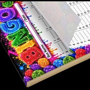 May include: A notepad with a colorful, neon-style graphic featuring the word BINGO in large, bubbly letters surrounded by dollar sign coins. The page includes a section labeled Box Name and Date, with a white grid area for tracking numbers.