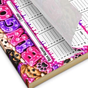 May include: A notepad for bingo games featuring a pink and purple gradient design with puppy illustrations, paw prints, and bones. The page includes fields for Date, Box Name, and numbered columns. One corner of the top sheet is folded over.