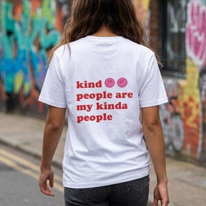 Könnte beinhalten: Ein weißes kurzärmeliges T-Shirt mit rotem Text auf der Rückseite, der "kind people are my kinda people" lautet, ergänzt durch zwei rosa Smiley-Symbole. Das T-Shirt wird mit einer dunkelgrauen Jeans kombiniert und ist von hinten zu sehen.