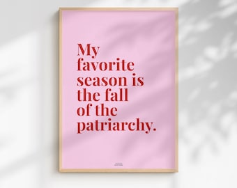 May include: A rectangular wall art print in a light wooden frame featuring a light pink background with bold red text that reads: My favorite season is the fall of the patriarchy. The design is centered on the print with a small credit line below.