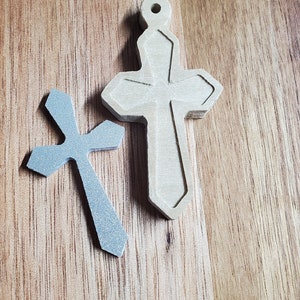 Può includere: Due croci di legno, una è di colore marrone chiaro e l'altra è di colore grigio blu chiaro. Le croci sono su una superficie di legno.