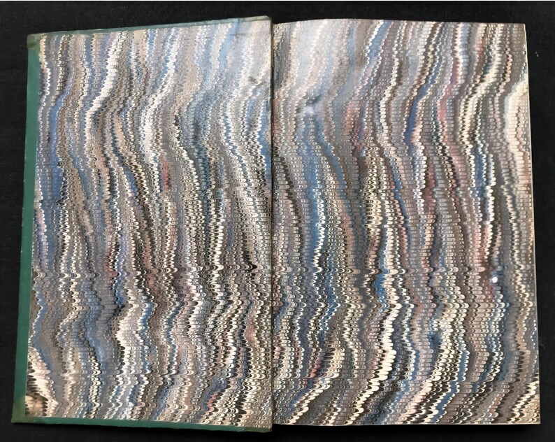 May include: Open book with marbled paper pages. The pages display a swirling pattern of blues, grays, and whites, creating a textured, wave-like effect. The book's spine is a muted green.