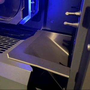 Puede incluir: Primer plano del interior de una caja de ordenador, que muestra un componente metálico negro con forma rectangular y un diseño ligeramente angulado. La caja presenta iluminación LED azul y varios puertos.