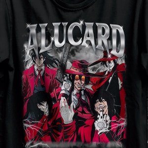 Può includere: T-shirt nera con la scritta "ALUCARD" in argento sopra una grafica di personaggi in rosso e nero. La maglietta è appesa a una gruccia nera contro un muro di mattoni scuri.