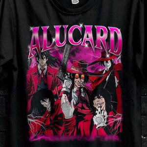 Può includere: T-shirt nera con grafica rosa dei personaggi di Alucard e la scritta "ALUCARD". La maglietta presenta anche testo promozionale e una farfalla.