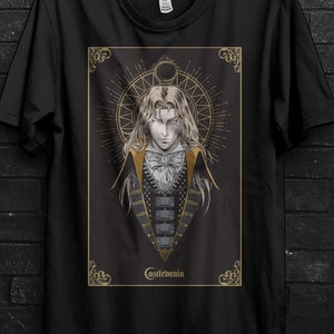 Può includere: T-shirt nero con un'illustrazione dettagliata di un personaggio di Castlevania. Il design include un ritratto con dettagli dorati e la scritta "Castlevania". La maglietta è appesa a una gruccia nera.