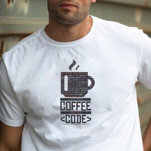 May include: White crew neck t-shirt featuring a coffee cup design made of code. The text "COFFEE <CODE>" is printed below the cup. The shirt is made of a soft material.