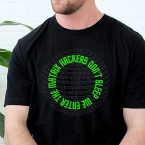 May include: Black t-shirt with a green circular graphic. The graphic features binary code and the text "THE MATRIX HACKERS DON'T SLEEP WE ENTER THE". The shirt is short-sleeved and appears to be made of cotton.