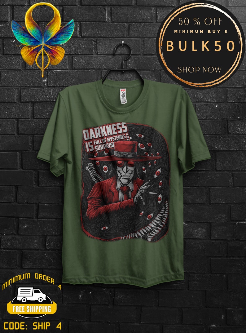 May include: Olive green t-shirt featuring a graphic of a character in a red suit and hat, surrounded by a dark, eye-filled design. The text "DARKNESS IS FULL OF MYSTERIES & SURPRISES" is displayed on the shirt.