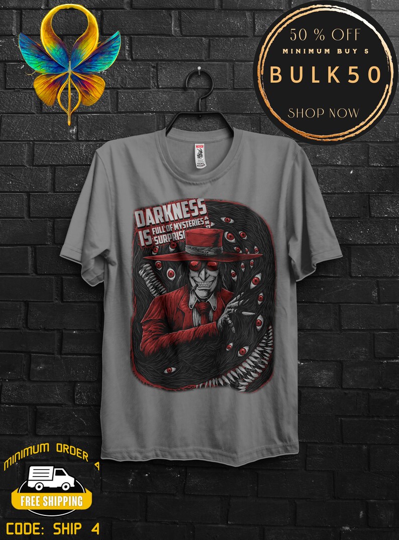 May include: Gray t-shirt featuring a graphic of a character in a red suit and hat, surrounded by black tentacles and red eyes. The text "DARKNESS IS FULL OF MYSTERIES & SURPRISES" is printed above the character. A black hanger is holding the shirt.