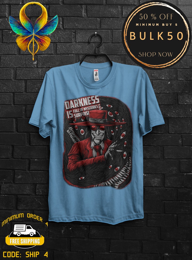 May include: Light blue t-shirt featuring a graphic of a character in a red suit and hat, surrounded by a dark, eye-filled design. Text on the shirt reads "DARKNESS IS FULL OF MYSTERIES & SURPRISES".