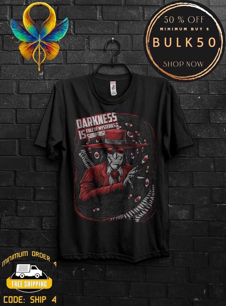 May include: Black t-shirt featuring a graphic of a character in a red suit and hat, surrounded by eyes and a dark, textured background. Text on the shirt reads "DARKNESS IS FULL OF MYSTERIES & SURPRISES."