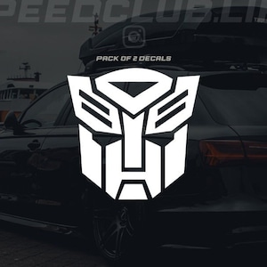 Może przedstawiać: Czarny samochód z białym naklejką z logo Transformers z tyłu. Naklejka zawiera napis "Pack of 2 Decals".