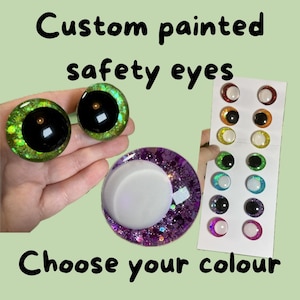 K&ouml;nnte beinhalten: Individuell bemalte Sicherheitsaugen in verschiedenen Farben. Das Bild zeigt zwei gro&szlig;e gr&uuml;ne und schwarze Augen, eine lila glitzernde Basis mit einem wei&szlig;en Deckel und eine Karte mit mehreren Augenfarben. Der Text lautet "W&auml;hle deine Farbe".