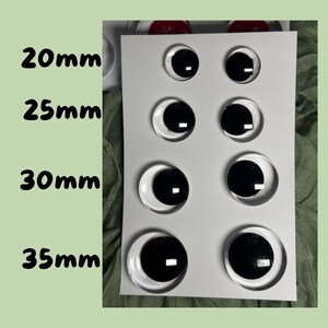 K&ouml;nnte beinhalten: Eine wei&szlig;e Karte zeigt acht klare, runde Wackelaugen mit schwarzen Pupillen. Die Gr&ouml;&szlig;en sind in schwarzer Schrift beschriftet: 20 mm, 25 mm, 30 mm und 35 mm. Die Augen sind in zwei Reihen zu je vier angeordnet.