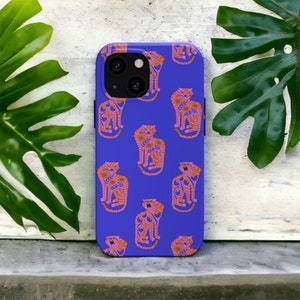 Może przedstawiać: Fioletowe etui na telefon z powtarzającym się wzorem stylizowanych pomarańczowych i różowych kotów. Etui ma wycięcie na aparat i czarną ramkę.