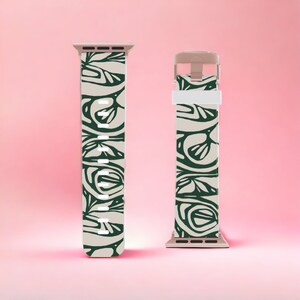 May include: Two beige and green patterned watch bands. The bands feature a repeating dark green leaf-like design on a beige background. The watch bands are displayed against a pink background.
