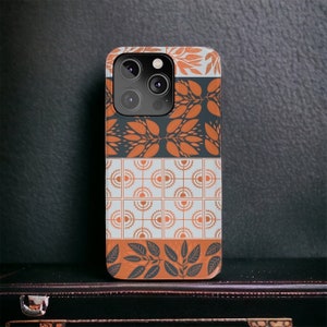 May include: A black phone case with a geometric pattern in shades of orange and white. The case has a camera lens cutout and a design of leaves in the bottom section.