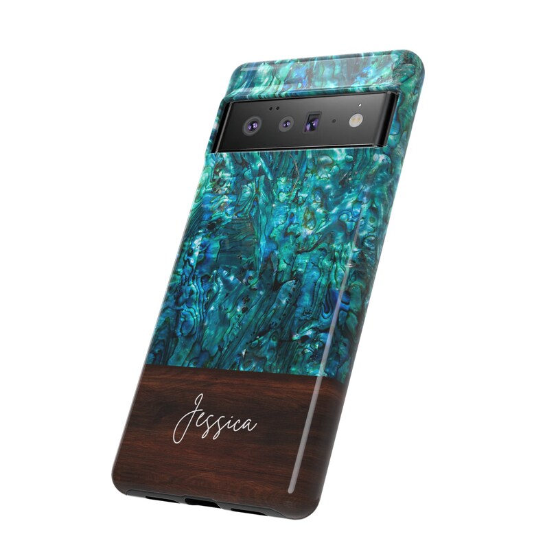 Może przedstawiać: Etui na telefon z wzorem muszli abalonowej w kolorze niebieskim i zielonym oraz brązowym drewnianym akcentem. Na etui widnieje napis "Jessica" w kolorze białym na drewnianym akcencie.