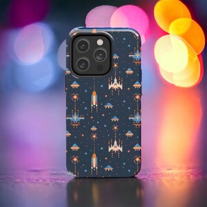 May include: A dark blue phone case with a pixelated space-themed design. The case features spaceships, rockets, and UFOs in shades of blue, orange, and white.