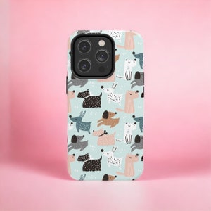 May include: A white phone case with a light blue background and a pattern of colorful cartoon dogs. The case has a black camera lens cutout.