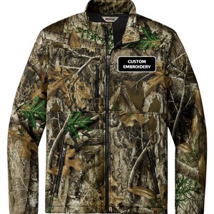 May include: A camouflage jacket with a full zipper, black accents, and the text "CUSTOM EMBROIDERY" on a black and white patch. The jacket features a high collar and multiple pockets, ideal for outdoor activities.