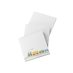 May include: White square notepads with a colorful train illustration at the bottom. The train features a green engine, yellow and green cars, and a blue caboose. The notepads are stacked at an angle.