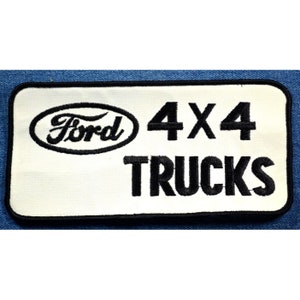 May include: White embroidered patch with black lettering that reads "Ford 4x4 Trucks". The Ford logo is a black oval with the word "Ford" in a white cursive font.