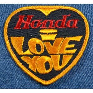 May include: A black heart-shaped patch with the word "Honda" in red embroidered lettering and the words "Love You" in gold embroidered lettering.