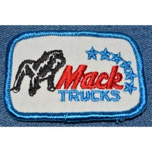 May include: A white embroidered patch with a blue border. The patch features a black gorilla, the red text "Mack" and the blue text "Trucks". There are five blue stars around the text.